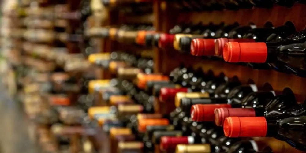 Row of wine bottles with red bottle caps on a wooden rack.