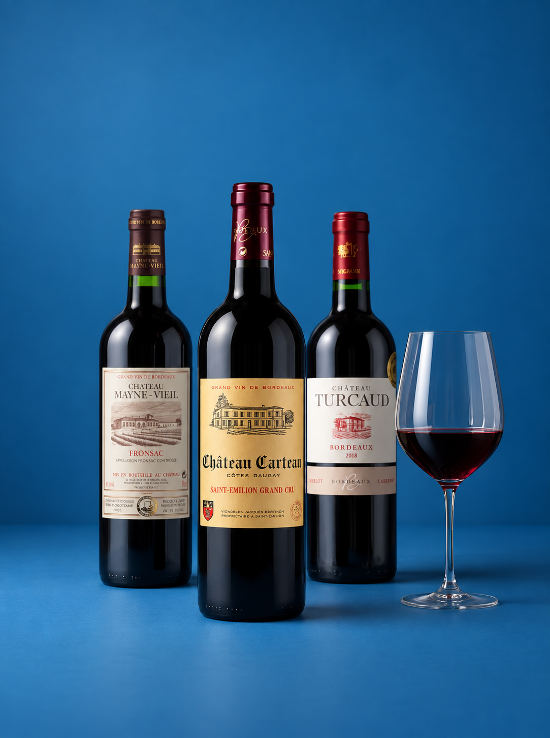 Three bottles of red wine and a filled wine glass on a blue studio background. The bottles include Chateau Marine-Vieille, Chateau Cartan, and Chateau Turcaud.