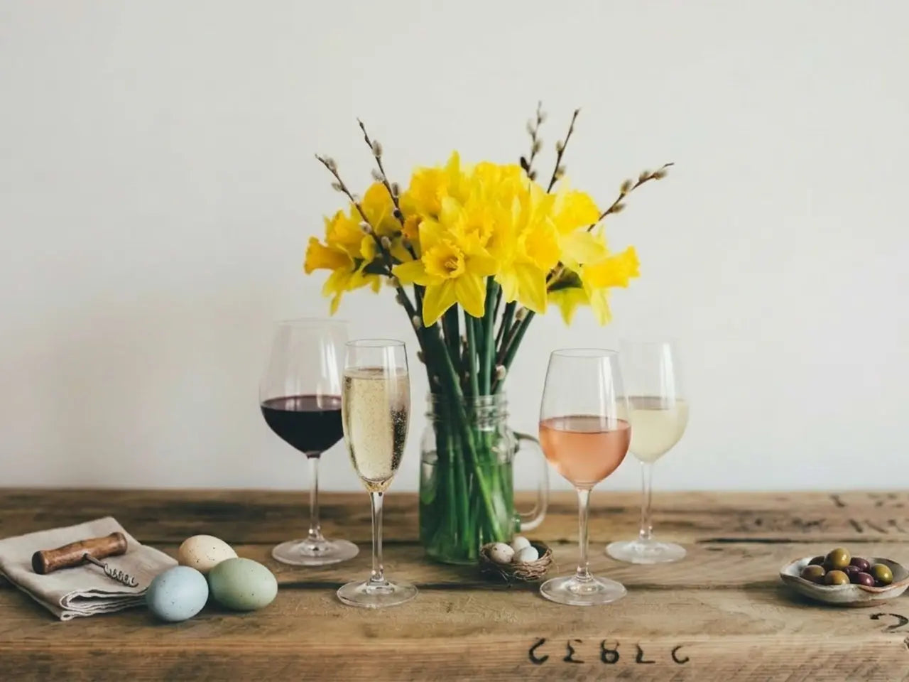 Table setting with yellow flowers, wine glasses, and Easter eggs on a wooden surface.