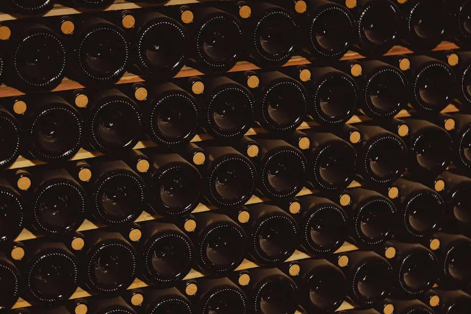 Stack of dark bottles with gold caps on a wooden shelf