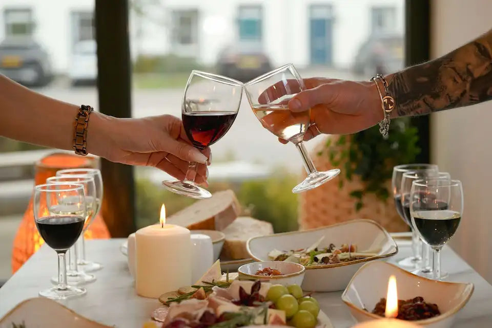 Two people clinking wine glasses at a dinner table with food and candles.