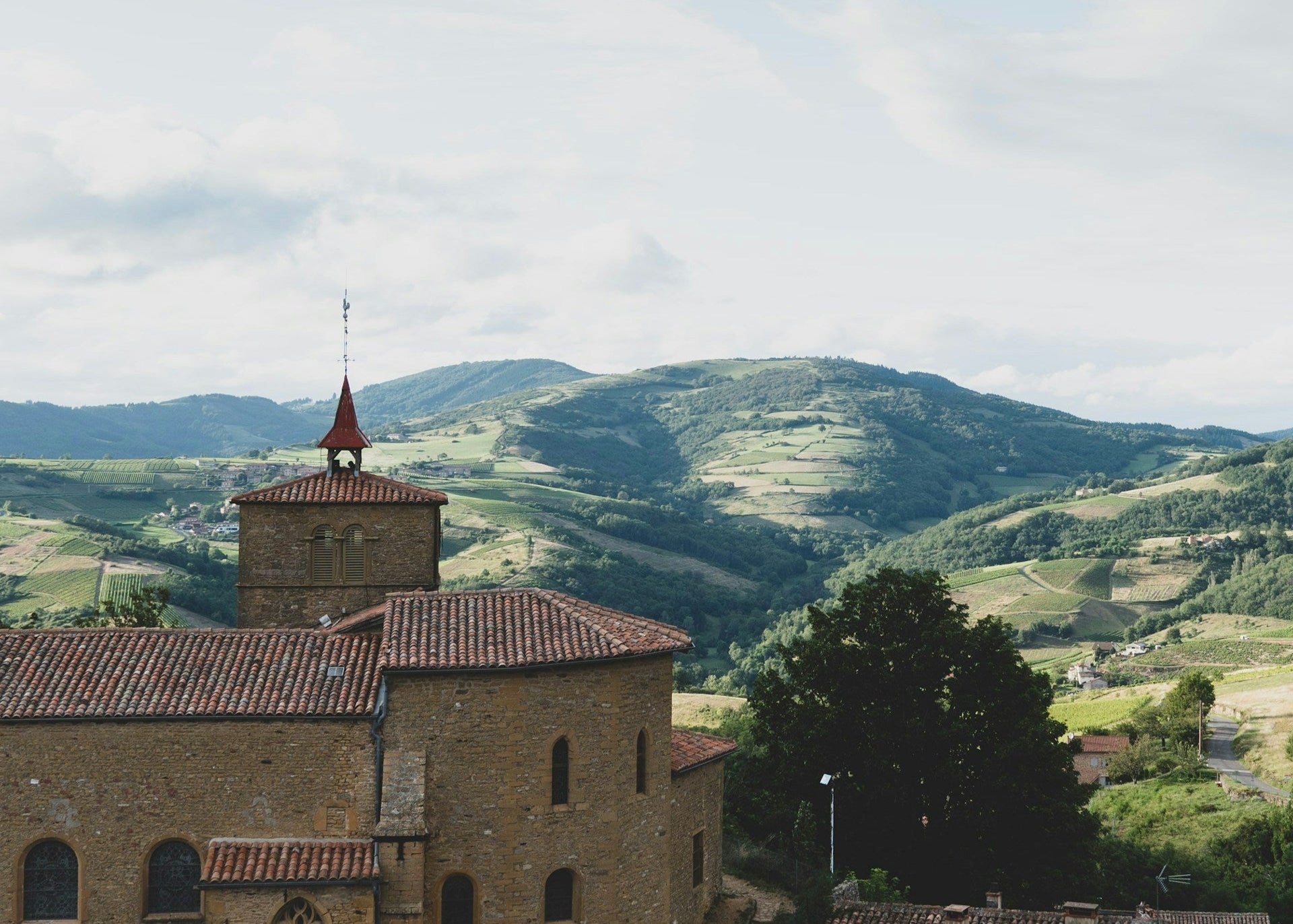 Historic building with a clock tower against a backdrop of green hills and blue sky.